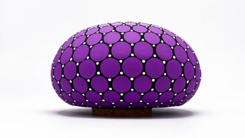May include: A purple ceramic egg with a black and white polka dot pattern. The egg is sitting on a cork base.