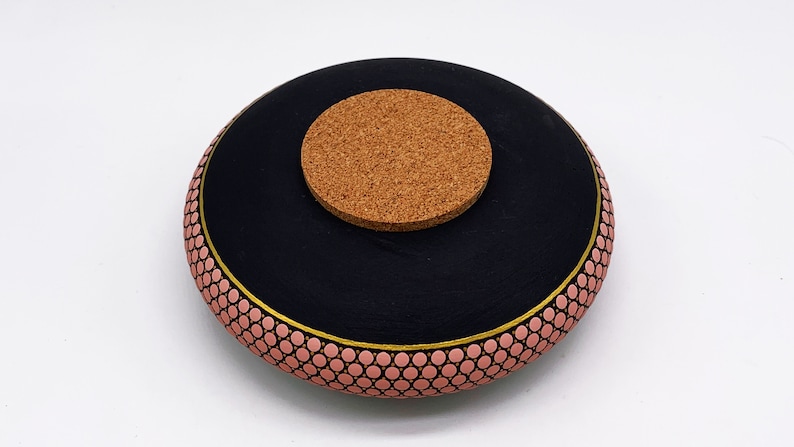 May include: Black ceramic bowl with a pink and gold geometric pattern. The bowl has a cork lid.
