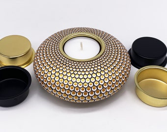 May include: A gold and white ceramic candle holder with a circular design. The holder has a small opening in the center for a tea light candle. The holder is surrounded by four smaller gold and black metal candle holders.