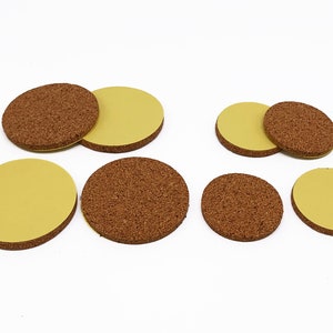 May include: A set of eight round cork furniture pads with adhesive backing. The pads are in two sizes, with the larger pads having a brown cork top and a yellow adhesive bottom. The smaller pads have a yellow adhesive top and a brown cork bottom.