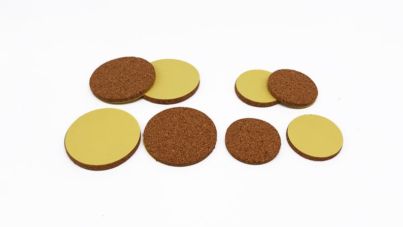 May include: A set of eight round cork furniture pads with adhesive backing. The pads are in two sizes, with the larger pads having a brown cork top and a yellow adhesive bottom. The smaller pads have a yellow adhesive top and a brown cork bottom.