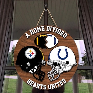 May include: Round wooden sign with the text "A HOME DIVIDED HEARTS UNITED". The sign features a football and two football helmets, one black and one white. The sign hangs from a jute rope.
