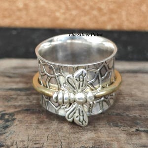 May include: A silver and gold spinning ring with a bee design. The ring has a honeycomb pattern and is made of sterling silver.