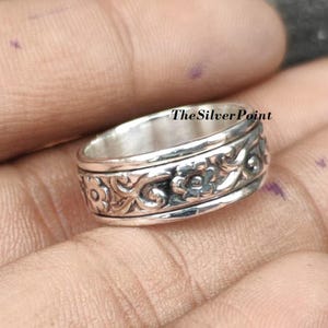 May include: A silver ring with floral and scrollwork designs. The ring has a textured band with repeating flower patterns and the text "The Silver Point". The ring is likely made of sterling silver.