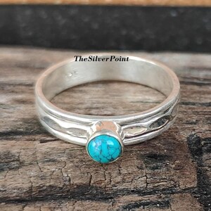 May include: A silver ring with a turquoise stone. The ring has a textured band and a bezel setting for the round, bright blue stone. The ring is displayed on a rustic wooden surface. The text "The Silver Point" is visible.