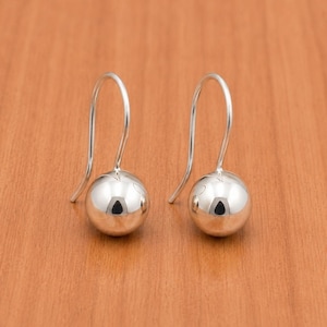 May include: A pair of silver-toned drop earrings featuring a smooth, polished spherical bead at the base of each curved wire hook. The earrings have a reflective, metallic finish and a simple, clean design that hangs vertically from the ear wire.