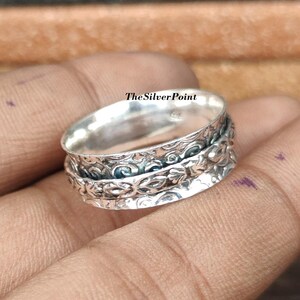 May include: A silver spinning ring with intricate floral designs. The ring is made of sterling silver and has a smooth, polished finish.