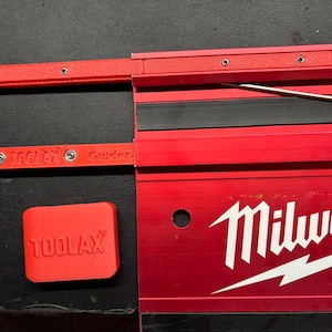 Può includere: Strumenti rossi con marchio TOOLAX e Milwaukee. L'immagine mostra uno strumento rosso con il logo TOOLAX, un pezzo quadrato rosso con il logo TOOLAX e uno strumento rosso con il logo Milwaukee. Gli strumenti sono su una superficie nera.