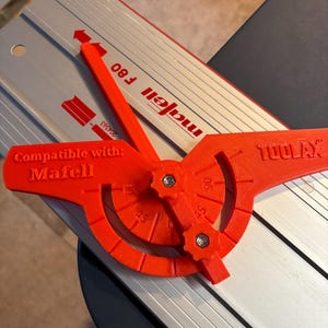 Può includere: Uno strumento rosso e argento con la scritta "TOOLAX" e "Mafell F80". Lo strumento ha una guida angolare regolabile rossa con indicazioni per 30, 45, 60 e 90 gradi. È visibile anche la scritta "Compatible con: Mafell".