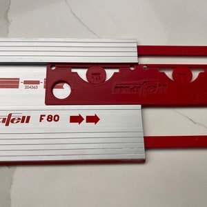 Puede incluir: Una guía de sierra Mafell F80 roja y plateada con un accesorio de plástico rojo etiquetado como "mafell" y "SAS".