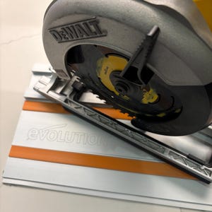 May include: A yellow and black DeWalt circular saw on a white and orange Evolution track saw guide. The saw blade is visible and has a black and yellow design.