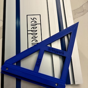 Könnte beinhalten: Ein blauer Kunststoff-Dreieckslineal mit dem aufgedruckten Wort "Scheppach". Das Lineal liegt auf einem silbernen und blauen Metalllineal mit dem aufgedruckten Wort "Scheppach".