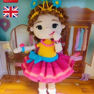 May include: A handmade crochet doll with a yellow top, pink skirt, and blue bow. The doll has brown curly hair, a flower crown, and pink shoes. It is a whimsical, handcrafted item.
