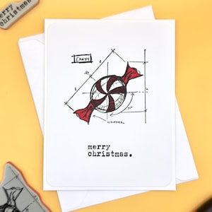Könnte beinhalten: Eine weiße Weihnachtskarte mit einer Süßigkeitenillustration und dem Text "merry christmas." Das Süßigkeitendesign hat eine rote Verpackung und eine schwarz-weiß gestreifte Mitte mit architektonischen Linien. Ein Stempel mit "merry christmas" ist sichtbar.