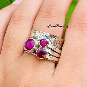 May include: A silver ring with three pink gemstones set in a textured band. The ring is worn on a finger.