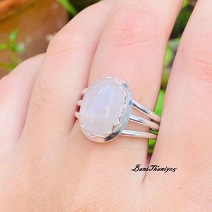 May include: A silver ring with a white oval gemstone. The ring has a delicate, intricate design and is set on a simple band.