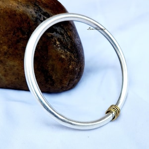 Op de afbeelding: Een zilveren armband met een gouden accent op de sluiting. De armband is dik en rond, en het gouden accent is gemaakt van meerdere kleine ringen.