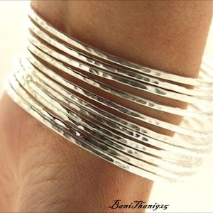 May include: A stack of 12 silver hammered bangle bracelets. The bracelets are thin and have a slightly textured surface.