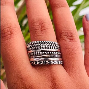 May include: A silver ring featuring multiple bands, each with a distinct textured design. The bands are stacked on top of one another, creating a unique and stylish look.
