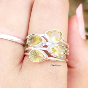 Könnte beinhalten: Ein Satz von vier Silberringen mit gelben birnenförmigen Edelsteinen. Die Ringe sind auf einem Finger übereinander gelegt.