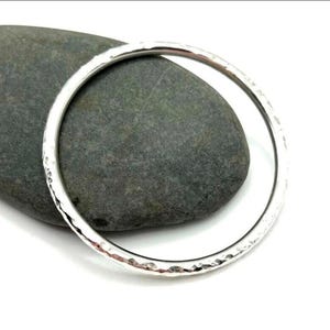 May include: A silver hammered bangle bracelet. The bracelet is round and has a smooth, polished finish.