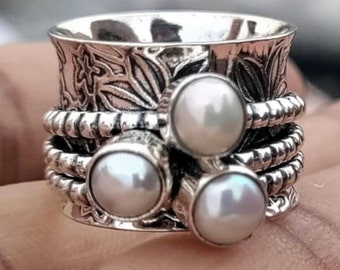 Könnte beinhalten: Ein silberner Drehring mit drei weißen Perlen. Der Ring hat ein strukturiertes Design und ist aus Sterlingsilber.