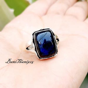 May include: A silver ring featuring a rectangular, dark blue cabochon gemstone set in a polished metal frame. The band has a split design on the sides. The text BaniThani925 is printed in black in the lower left corner of the image area.