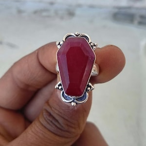 Puede incluir: Un anillo de plata con una piedra preciosa roja en forma de ataúd.