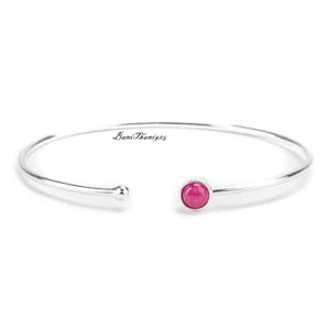 May include: A silver bangle bracelet with a single pink gemstone in the centre.