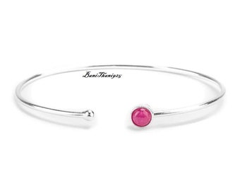 May include: A silver bangle bracelet with a single pink gemstone in the centre.