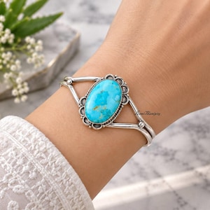 May include: A silver cuff bracelet featuring a large, oval-shaped turquoise stone with brown matrix veining. The stone is set in a decorative scalloped silver bezel with a twisted wire border, attached to a split-shank silver band with small spheres.
