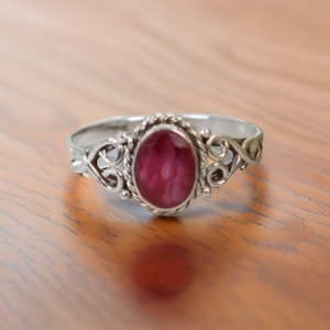 May include: A silver ring with a pink oval gemstone set in a decorative filigree design.
