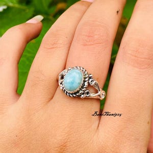Könnte beinhalten: Ein silberner Ring mit einem hellblauen ovalen Edelstein, der in einem filigranen Design eingefasst ist.