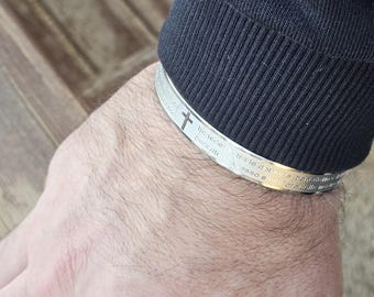 Op de afbeelding: Zilveren armband met een kruis en de inscriptie "Wees sterk en moedig" in het Engels en Hebreeuws.