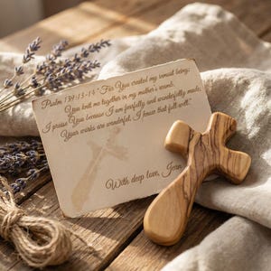 Peut inclure: Une croix en bois avec une finition naturelle est posée sur une surface en bois à côté d'une carte avec une écriture. La carte contient une citation du Psaume 139:13-14 et les mots "With deep love, Jean." Un bouquet de lavande et de la ficelle sont également présents.