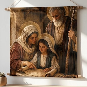 May include: A rectangular wall hanging featuring a printed illustration of a family of three with golden halos. The figures are dressed in earth-toned robes and are gathered around an open scroll. The hanging is suspended by a wooden rod.