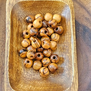 May include: A wooden bowl filled with round, brown wooden beads with dark brown stripes. The beads have a hole in the center for stringing.