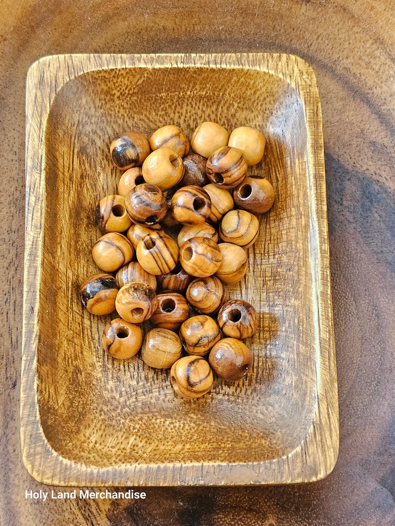 May include: A wooden bowl filled with round, brown wooden beads with dark brown stripes. The beads have a hole in the center for stringing.