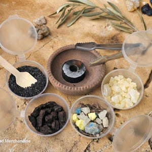 May include: An assortment of incense ingredients, including black granules, resin, and colorful stones, are displayed in clear containers with lids. A small wooden scoop and metal tongs are also included. A small clay bowl holds a charcoal disc.