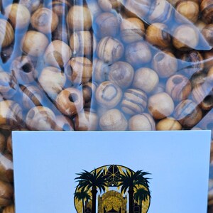 May include: A close-up of a bag of olive wood beads. The beads are a light brown color with dark brown stripes. The bag is clear plastic and has a certificate that says "HolyLandMerchandise" and "This certificate hereby verifies that this item is made from 100% authentic Bethlehem Olivewood which was..."