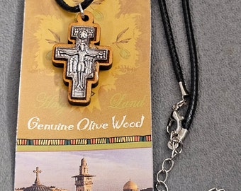 May include: A silver and wood cross pendant on a black cord necklace. The pendant is made of olive wood and features a silver crucifix. The necklace is packaged on a card with a picture of Jerusalem and the text "Genuine Olive Wood".
