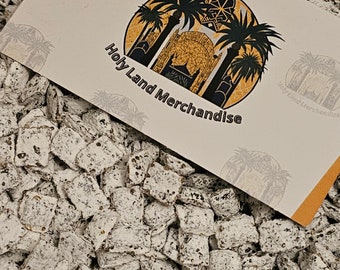 May include: A close-up shot of a pile of white and brown speckled treats, with a card on top. The card features a circular logo with palm trees, a building, and the text "Holy Land Merchandise".