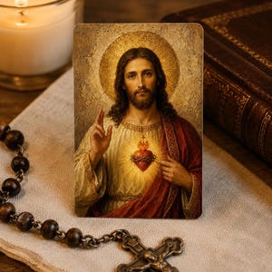 May include: A rectangular religious prayer card featuring a portrait of Jesus Christ with a golden halo, wearing a white tunic and red mantle, pointing to a glowing Sacred Heart. The image displays a classic artistic style with warm, muted tones.