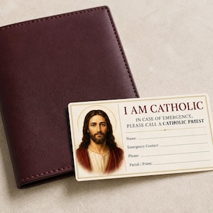 May include: A dark burgundy leather-like wallet next to a rectangular white card featuring an illustration of Jesus Christ and the text: I AM CATHOLIC, IN CASE OF EMERGENCY, PLEASE CALL A CATHOLIC PRIEST, with blank lines for Name, Emergency Contact, Phone, and Parish/Priest.