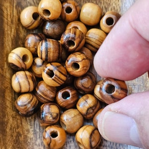 May include: A bowl of brown and tan wooden beads with a hole in the center of each bead. The beads are in a wooden bowl.