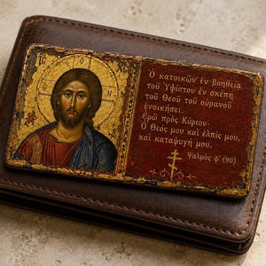 Puede incluir: Una cartera de cuero marrón oscuro con una placa rectangular en la parte frontal. La placa muestra un icono dorado de Jesucristo a la izquierda y texto en griego sobre un fondo rojo oscuro a la derecha, incluyendo la referencia al Salmo 90.