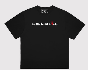 Può includere: Maglietta nera con testo bianco che recita "Le Monde est à Nous" con una "N" rossa.