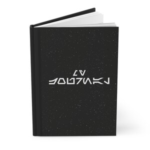 May include: A black notebook with a white starry sky design and the text "LV 426" in white.