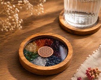 May include: A wooden coaster with a clear resin centre filled with colourful crystals arranged in a rainbow pattern. A copper-coloured emblem is in the centre. A glass of water sits on a matching wooden coaster.