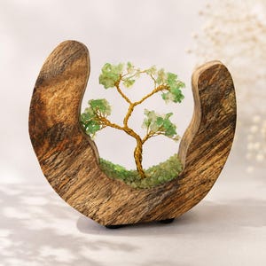 May include: A crescent-shaped wooden sculpture featuring a wire-wrapped tree with green gemstone leaves. The base of the tree is filled with small green stone chips, and the entire structure is supported by a curved, textured natural wood frame.